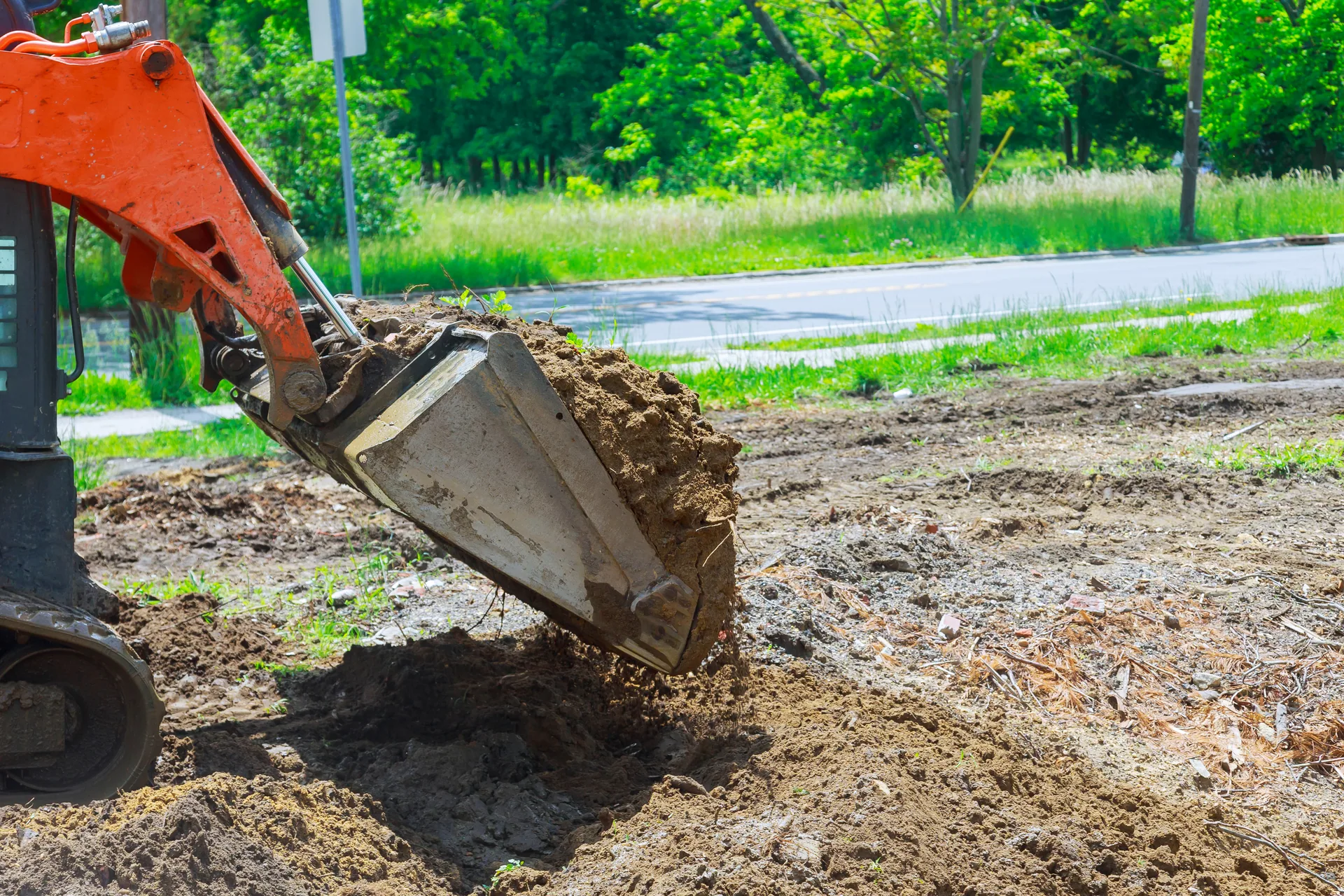Excavator bucket dumping soil roadside site preparation