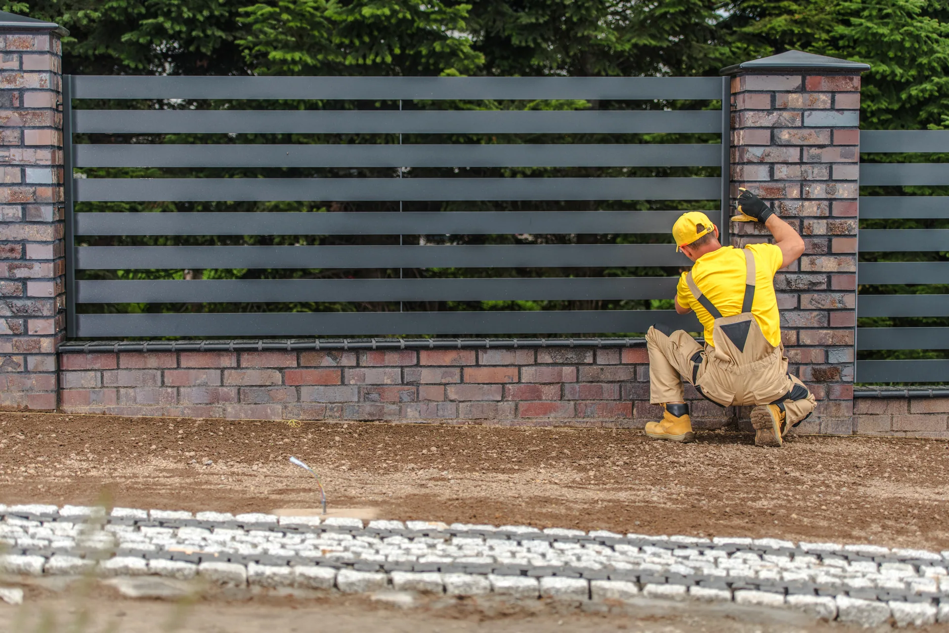Worker installing horizontal slat metal fence brick pillars