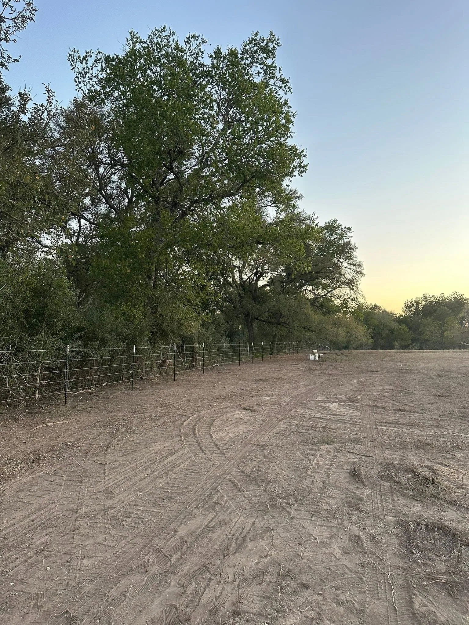 Dusk tire tracks cleared field t post fence tree line central texas