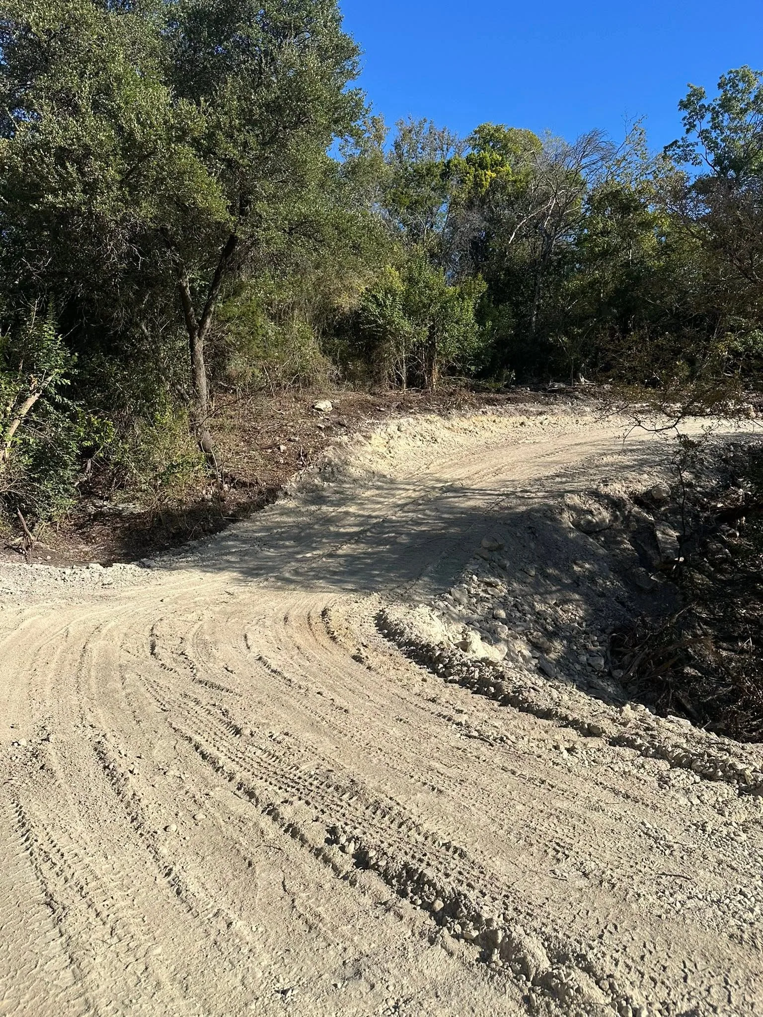 Freshly graded limestone caliche access road curve tire tracks hill country