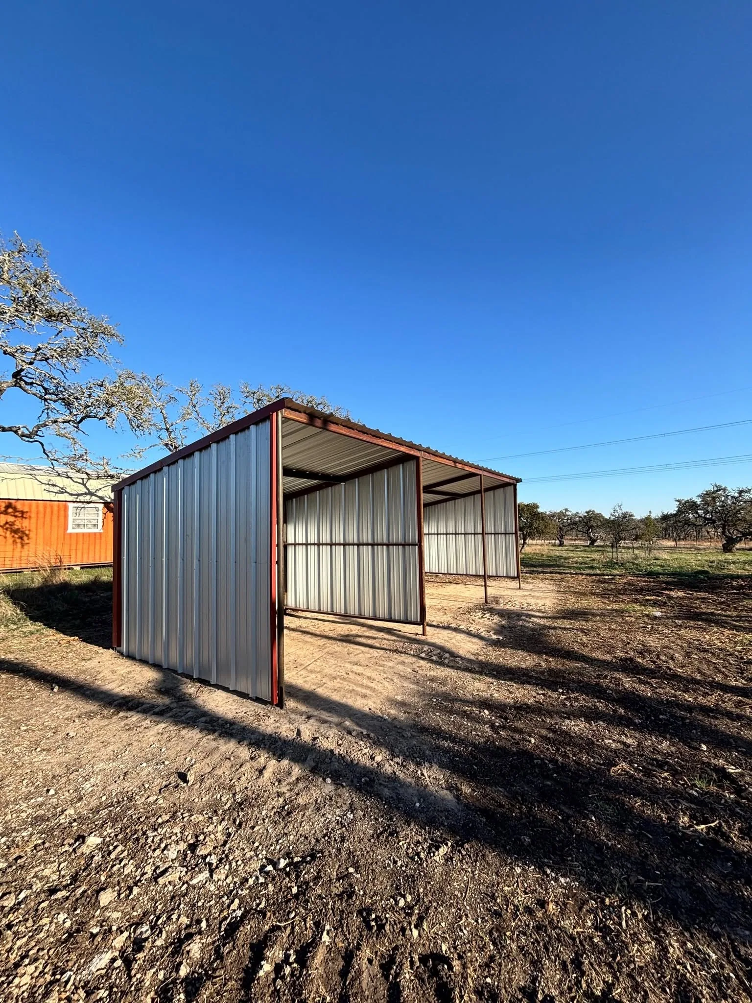 Low angle two bay metal loafing shed clear blue sky oak pasture texas