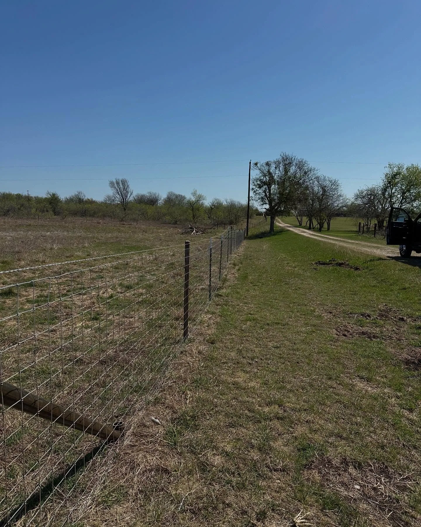 New woven wire fence line wood posts dirt ranch road clear sky