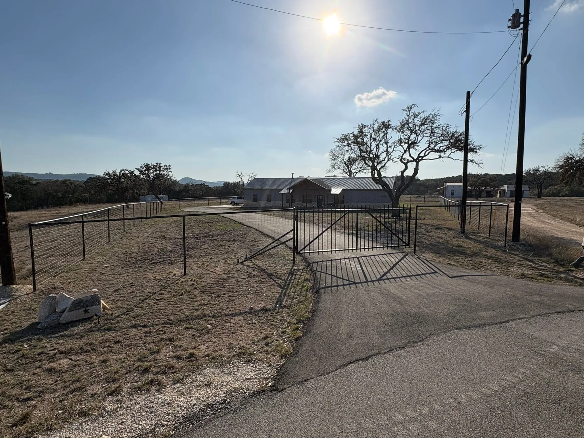 Open black pipe entry gate hog wire fence stone ranch house hill country