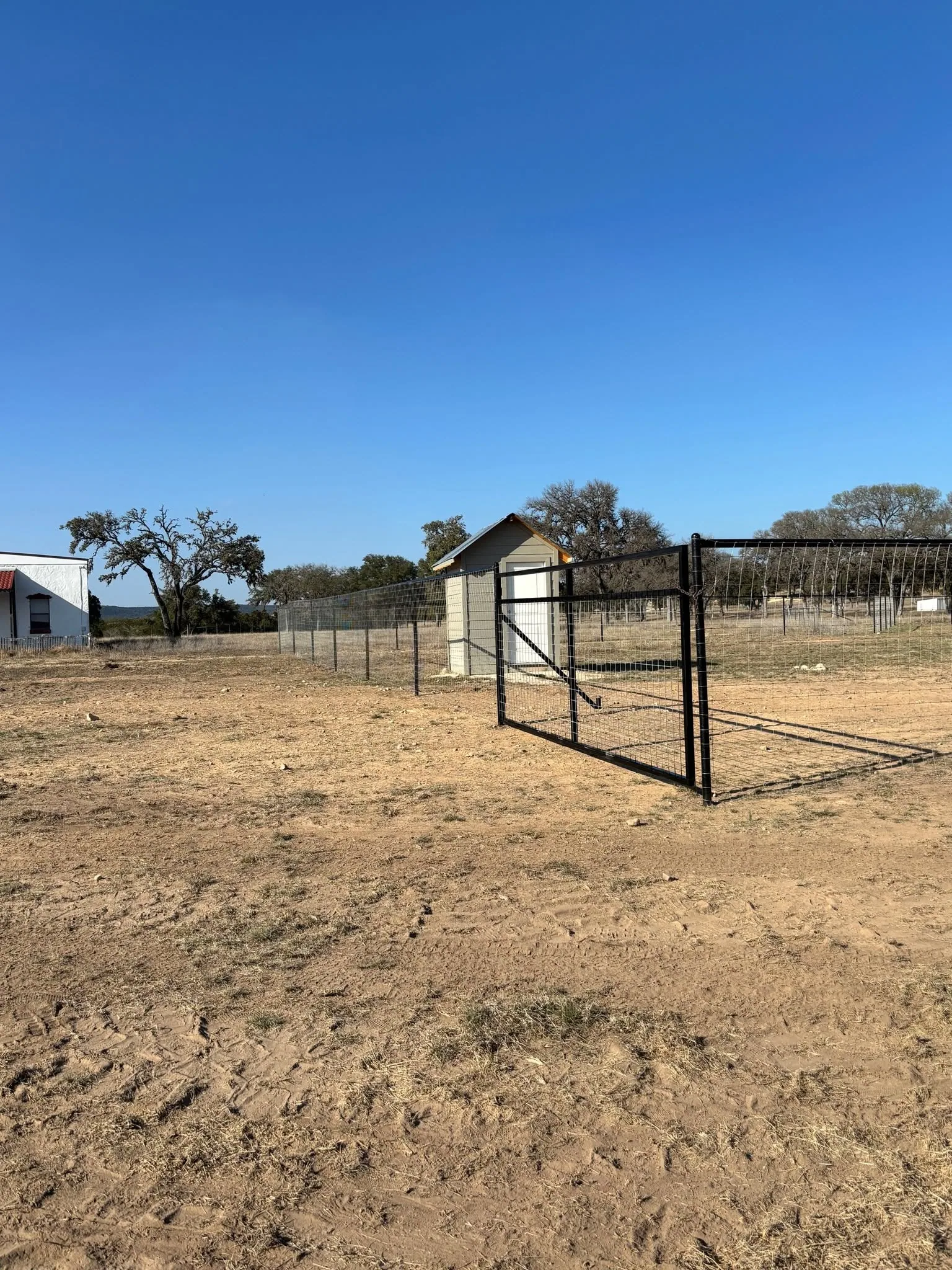 Open black pipe gate wire mesh fence small shed bare dirt lot texas