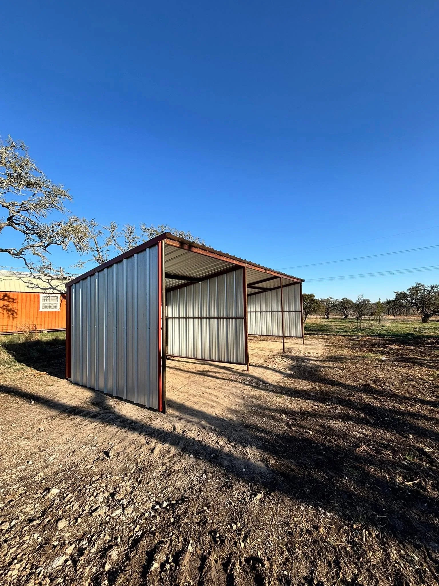 Open front metal loafing shed red trim graded pad hill country