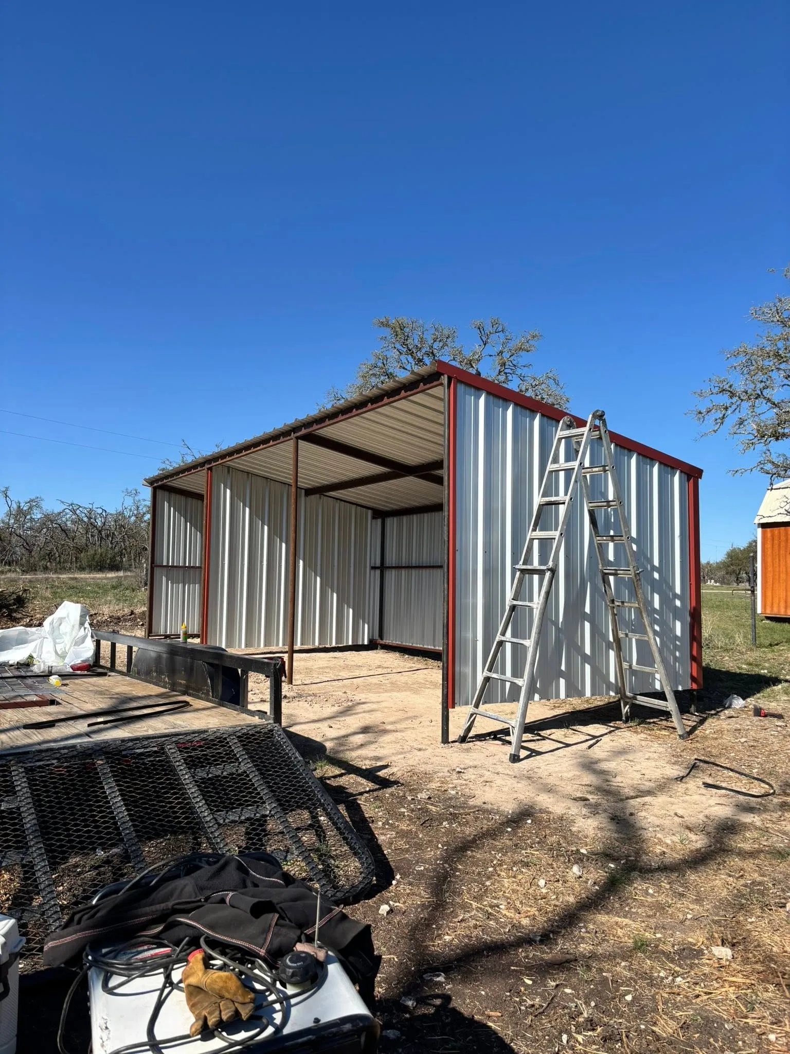 Open front metal loafing shed red trim ladder hill country build