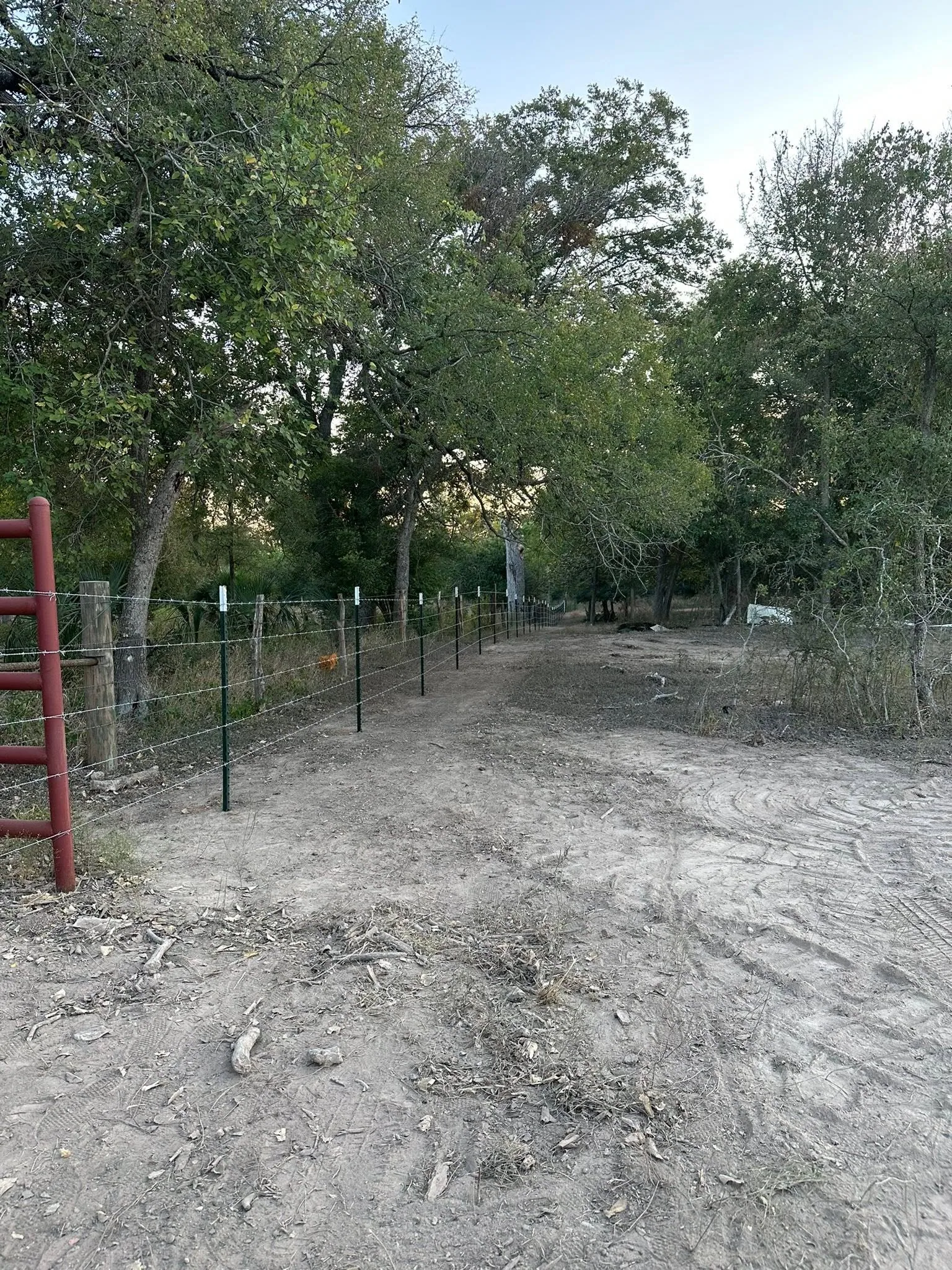 Red pipe gate barbed wire fence cleared dirt lane tree line