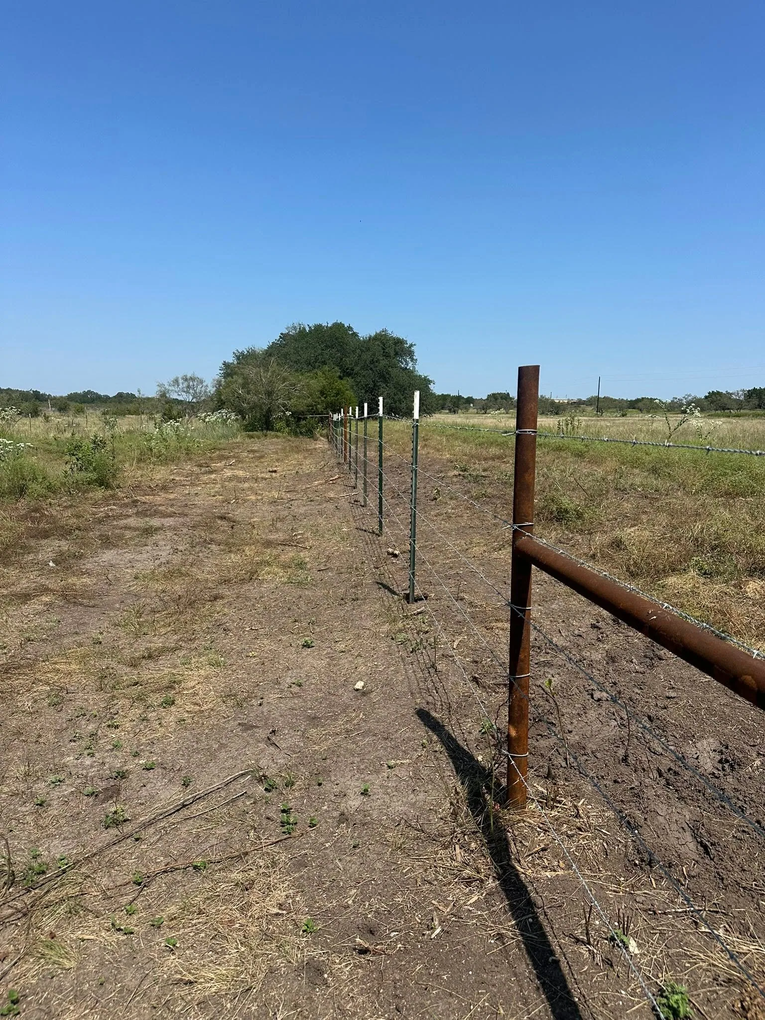 Rusty pipe corner post barbed wire t post fence cleared strip texas