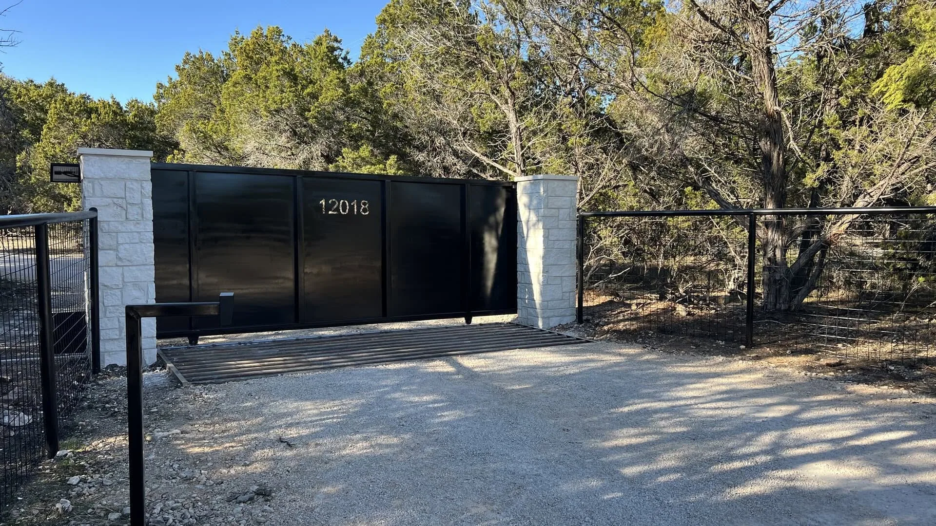 Solid black steel slide gate cattle guard limestone pillars hill country