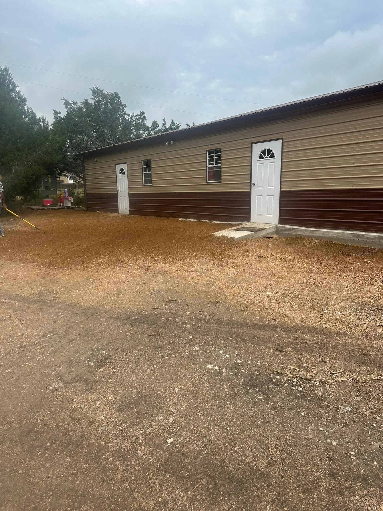 Two tone tan brown metal building raked dirt pad two white doors