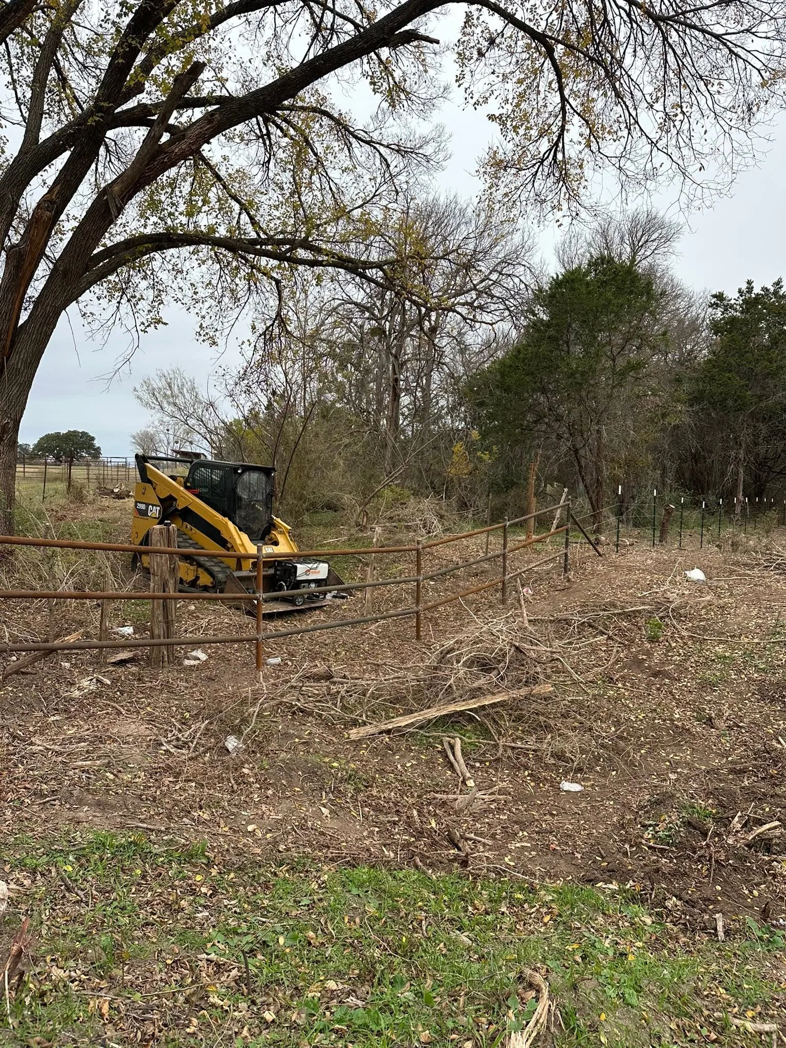 Yellow cat skid steer behind pipe rail fence cleared brush pile central texas